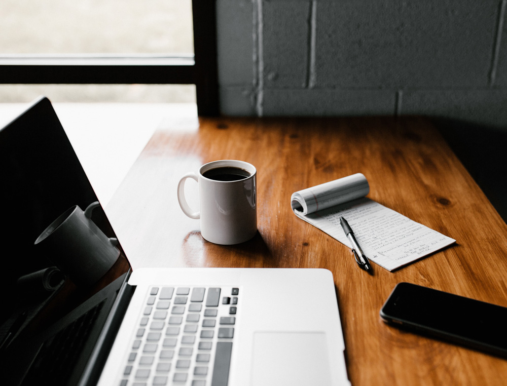 laptop, coffee mug, notebook, and smartphone