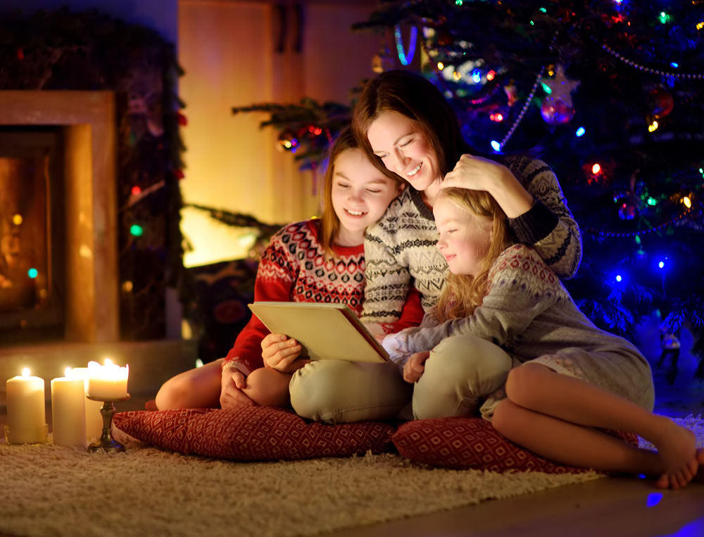 Mother and two girls watching a holiday movie on a tablet by the fireplace