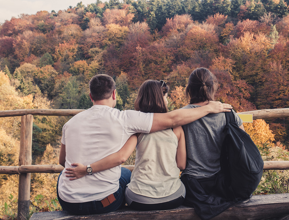 a man hugs two women on a bench in the fall