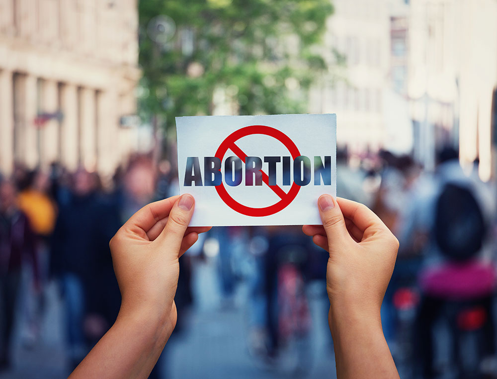 person holding up a ban abortion sign with crowd in the background
