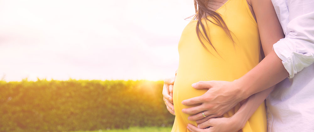 pregnant wife in yellow dress being hugged by husband outside in beautiful landscape