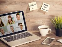 home office with open laptop showing team meeting, cup of coffee, and cell phone