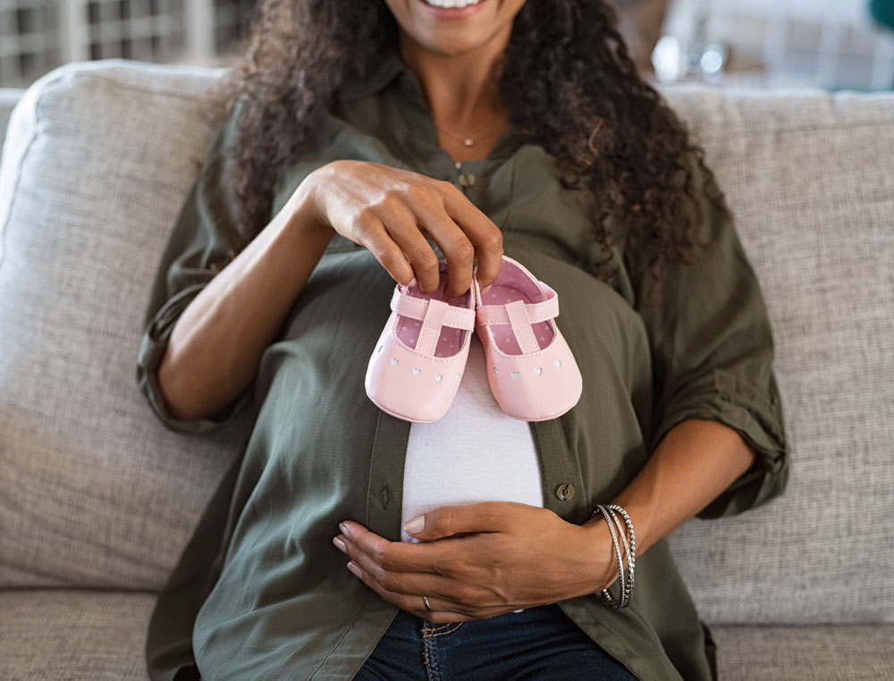 pregnant black woman holding pink baby shoes