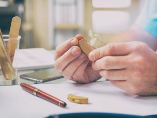 A hearing specialist holds a modern hearing aid in their hands. 