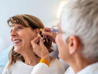 A patient at Elite Hearing has her hearing aid adjusted by a professional. 