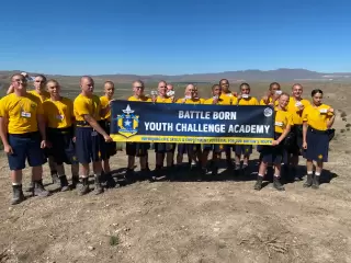 The image shows eager students and faculty members displaying the Battle Born Youth Challenge Academy flag.