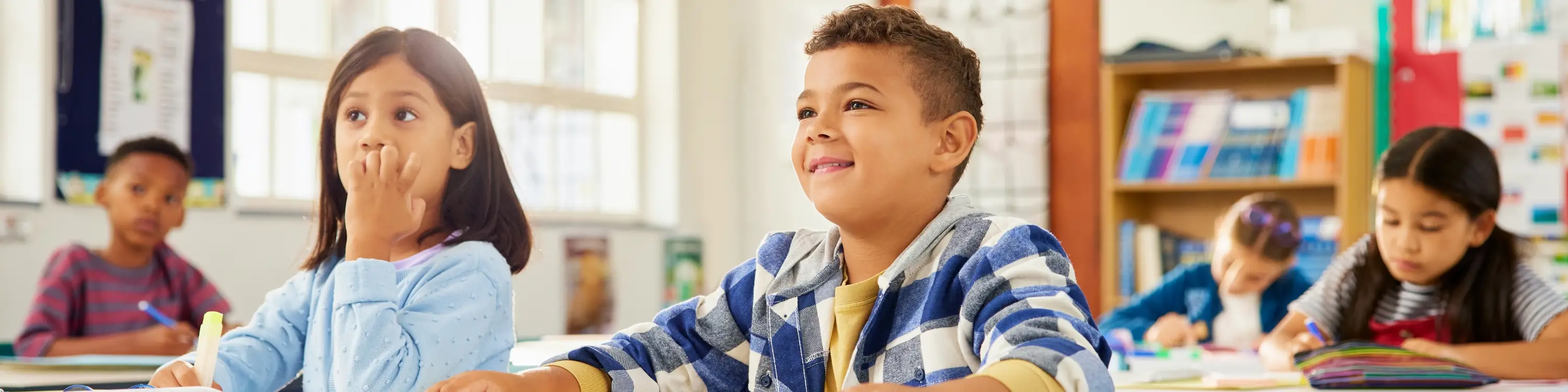 Young boy smiling while in his classroom with his other classmates.