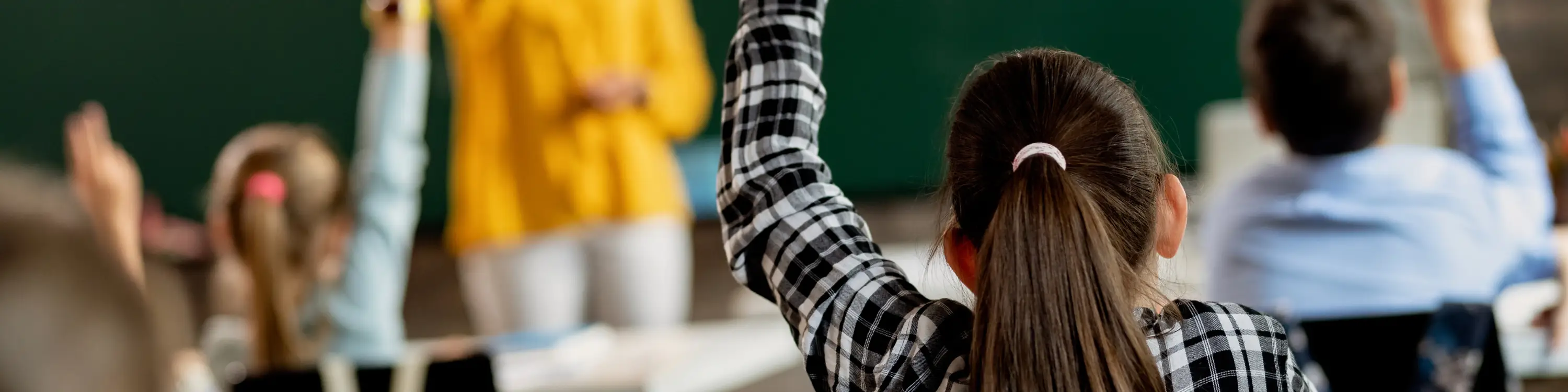 Young student raising her hand in a classroom.