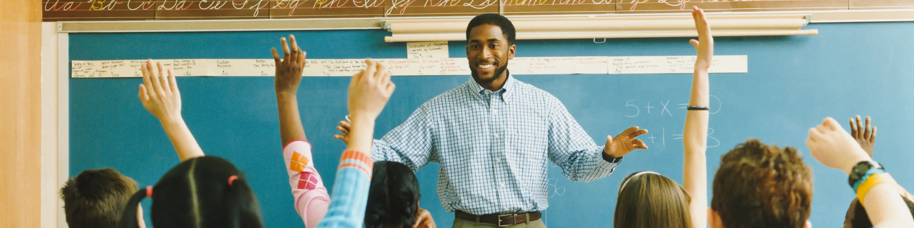 Young smiling teacher looking on his students who are raising their hands.