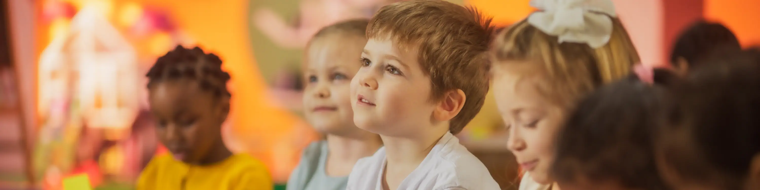 Young classroom students looking to the left and listening to their teacher.