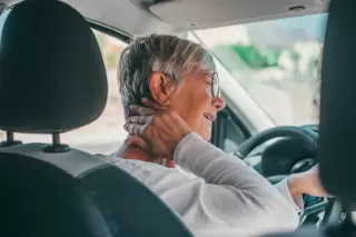 an older woman in the driver's seat of a car holding her neck in pain after an accident in New Mexico