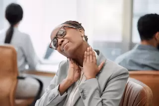 a woman in a gray suit holding her neck in pain after a neck injury due to an accident in texas