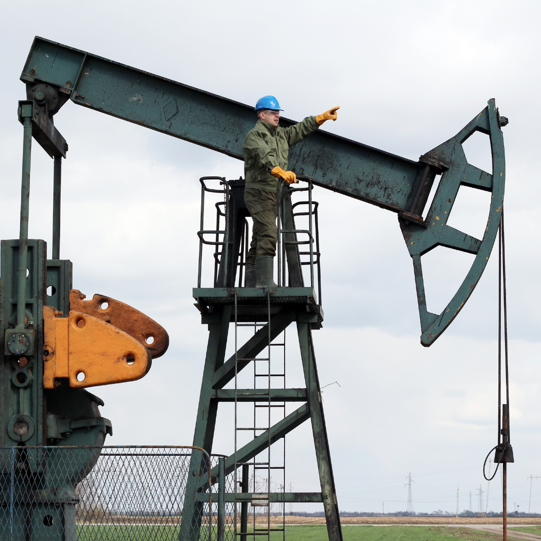 Man with safety hat on standing on a platform next to an oil derrick