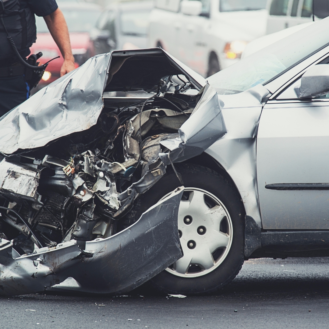 Car with crash damage and a police officer standing next to it