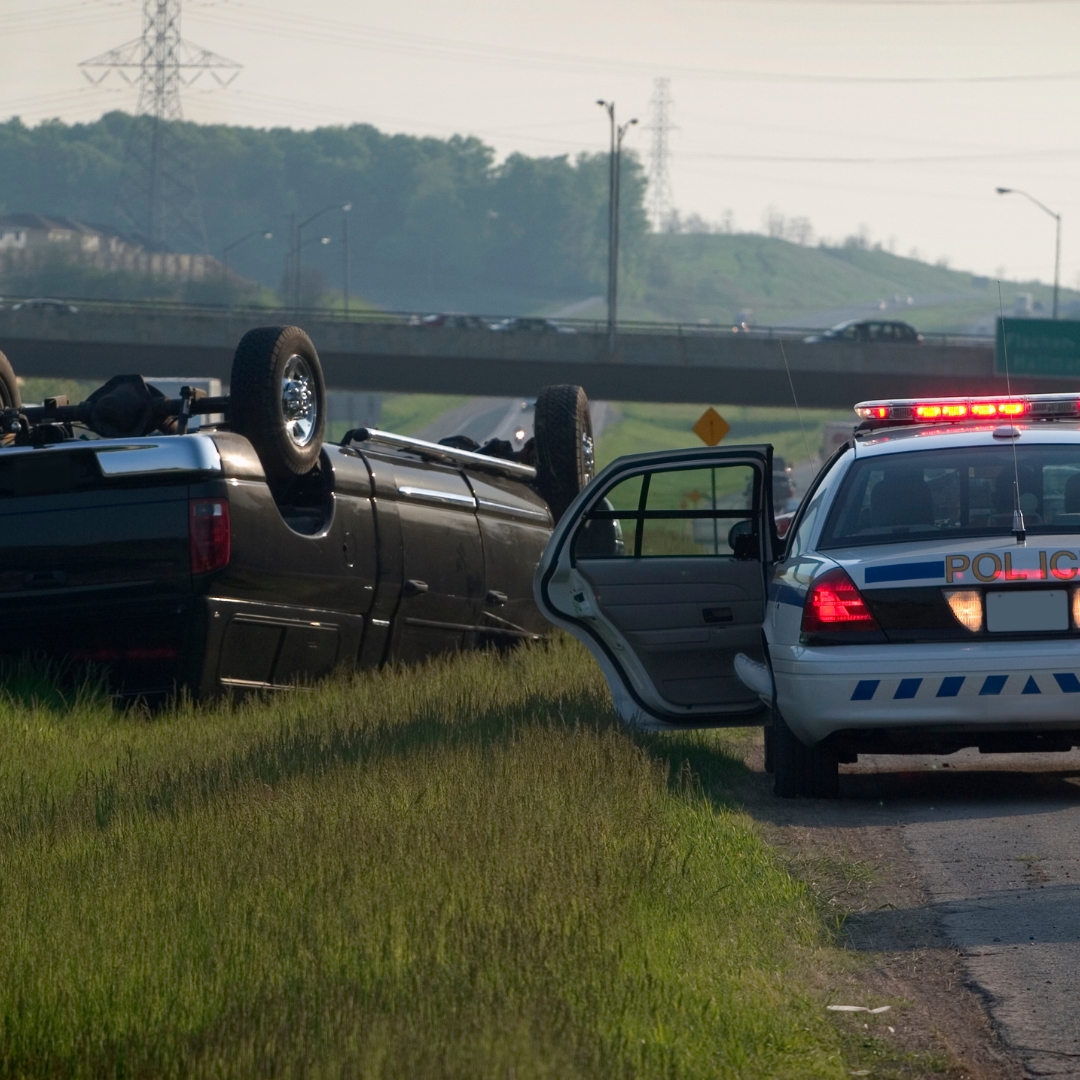 vehicle flipped over on side of the road next to a police car