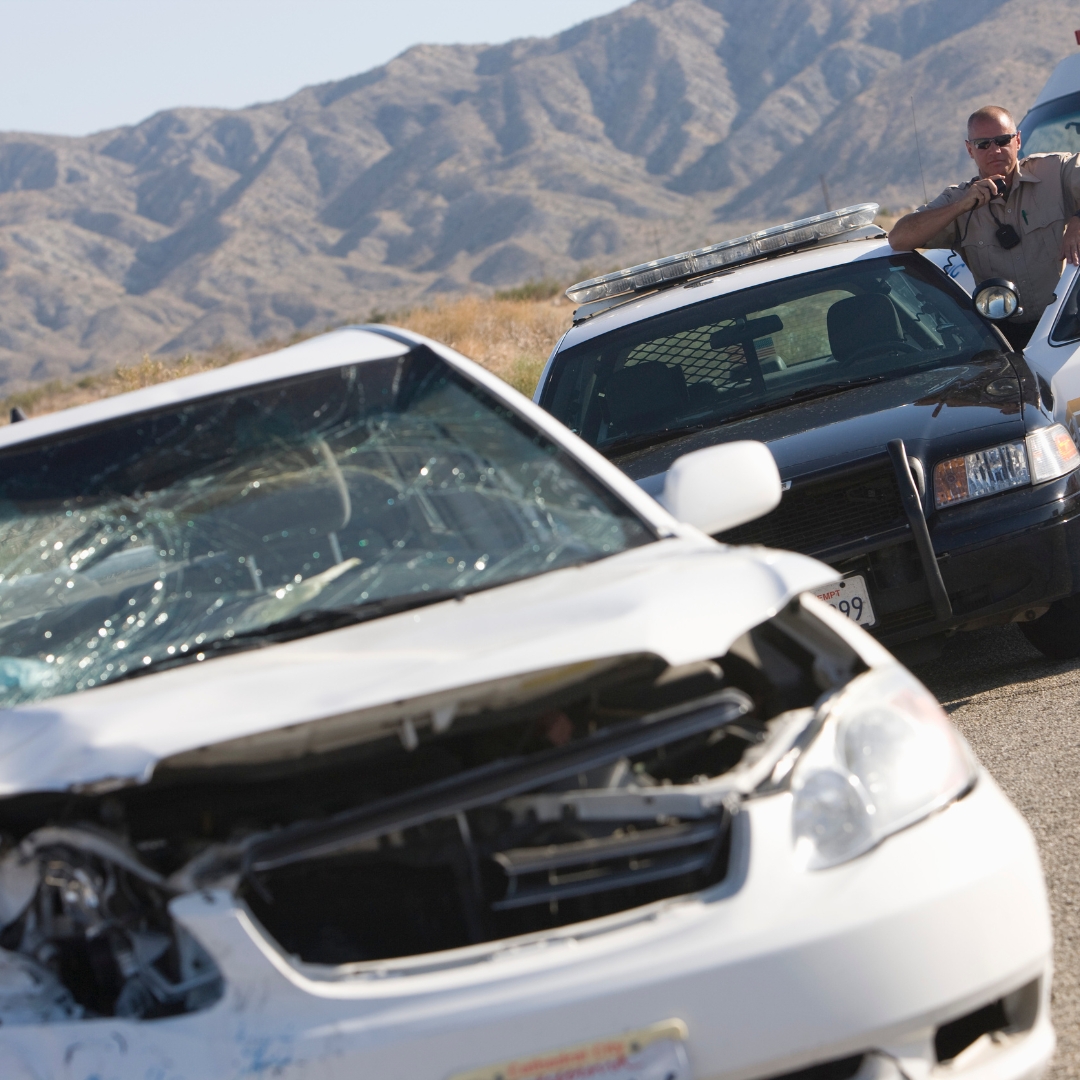 A white car with crash damage in front of a police car