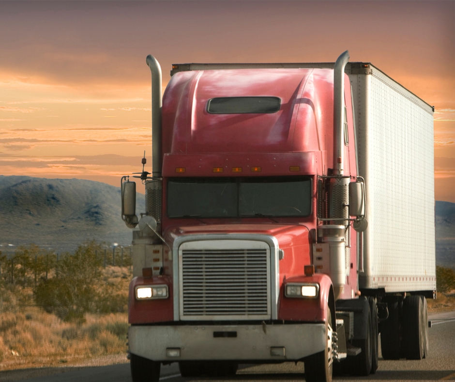 Red semi truck on a highway at sunset